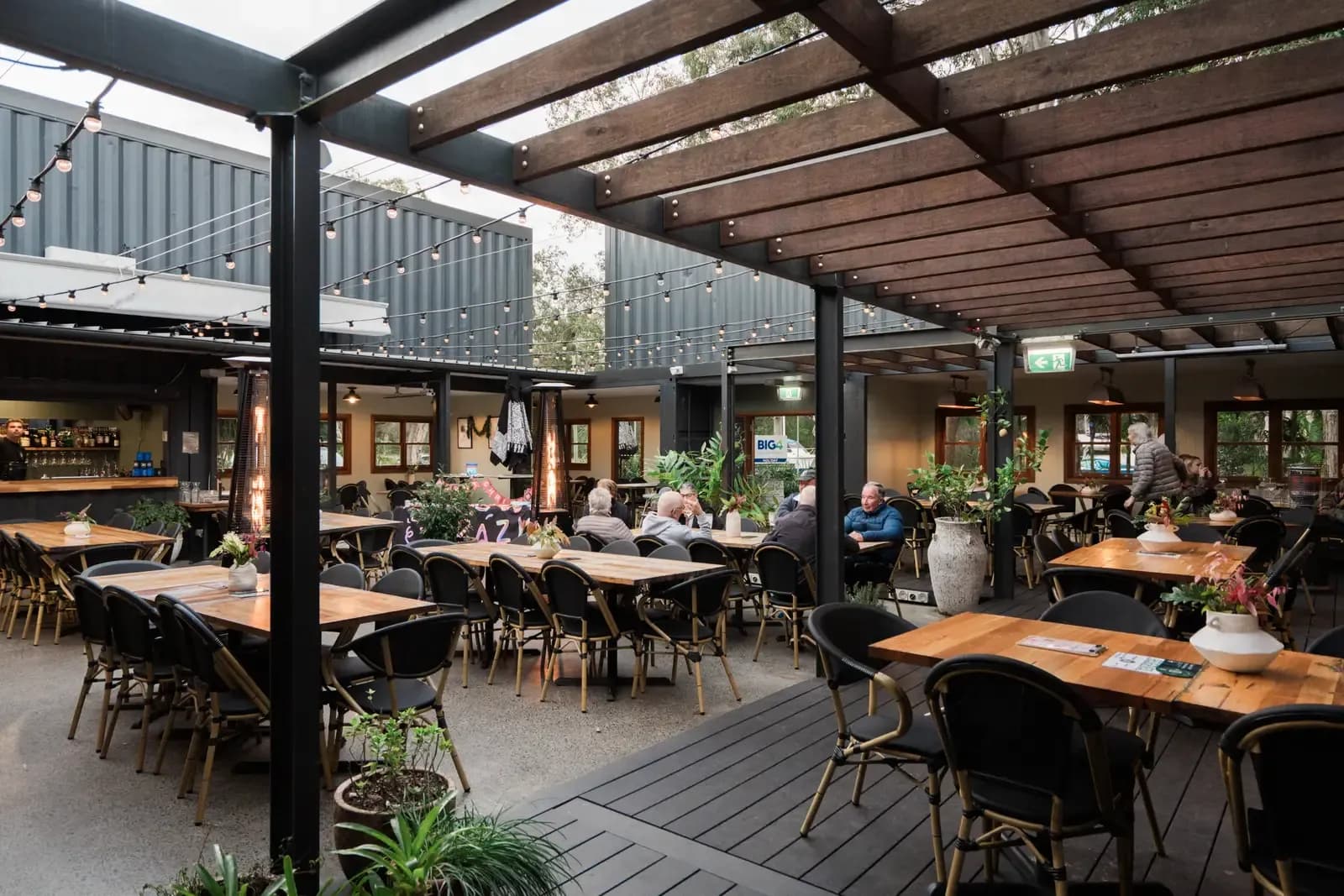 The courtyard at The 383 Wooli under the timber pergola, with string lights and tables set for guests